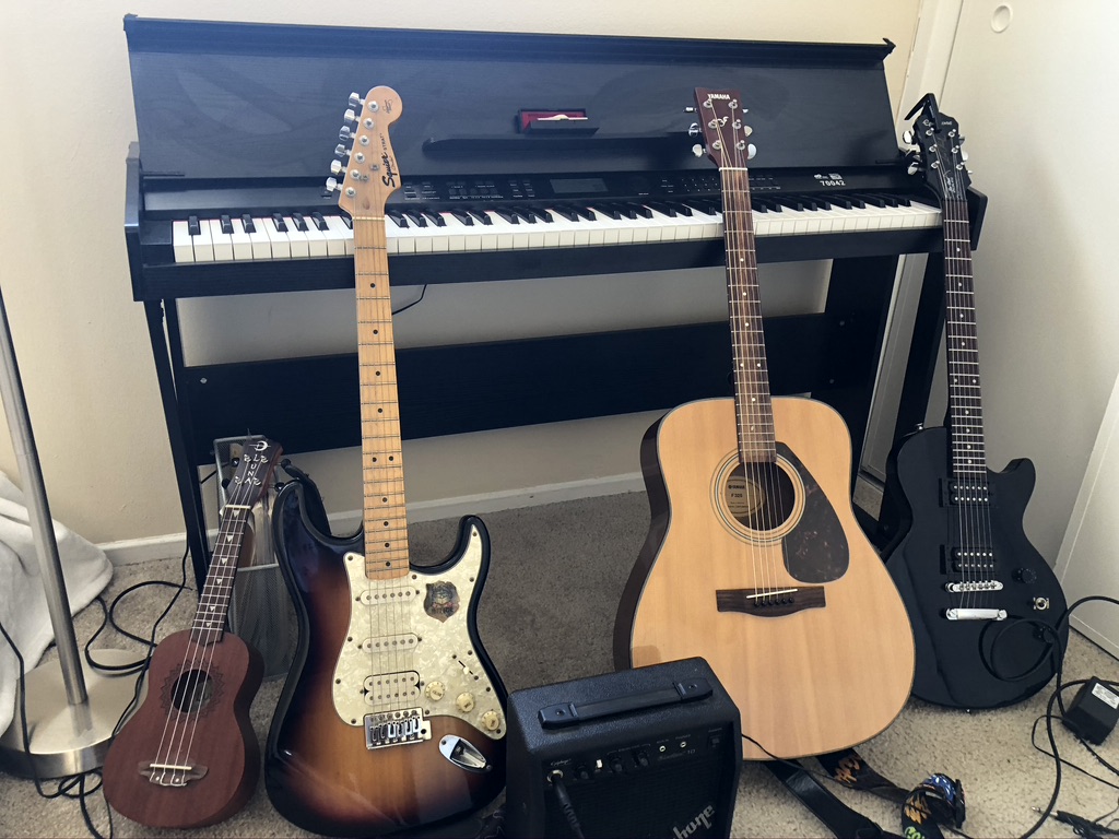 A digital piano, two electric guitars, an acoustic, a ukulele, and a Hape amp